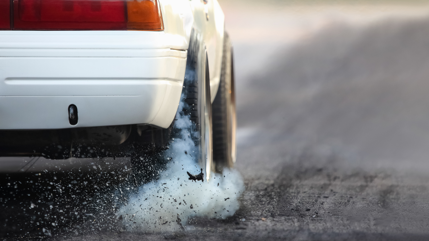 Rear tire of a white car skidding on a wet road, spraying water and smoke