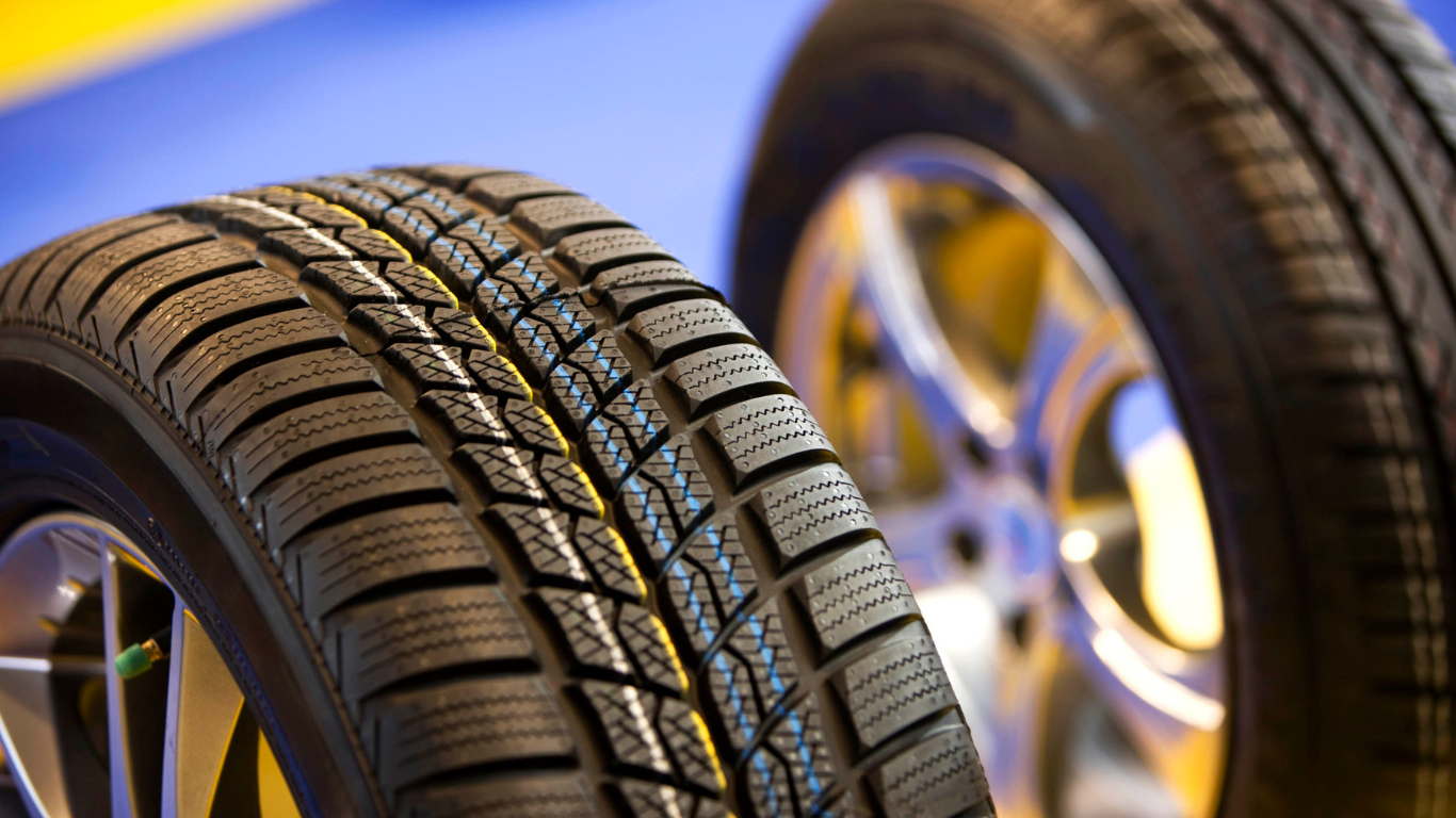 Close-up of two car tires, one in focus with deep tread, beside a blurred alloy wheel