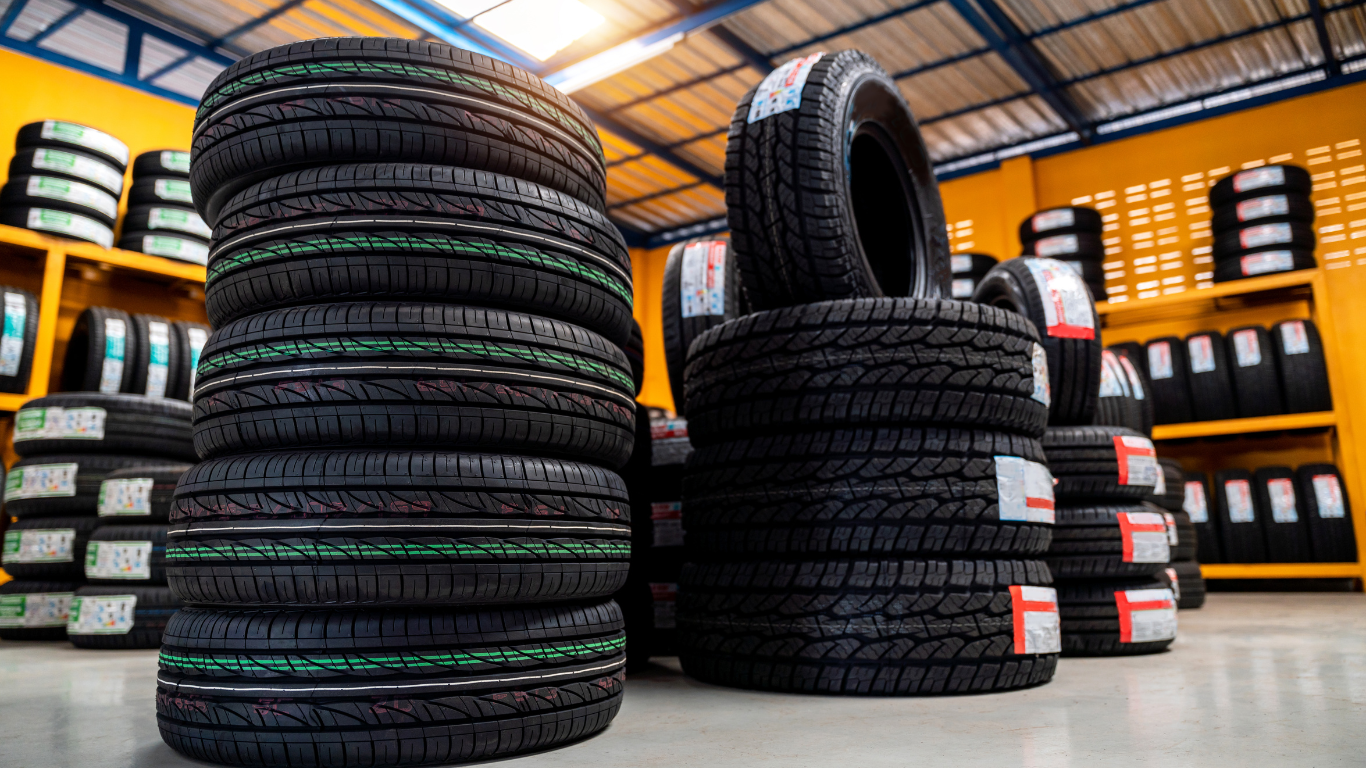 Stacks of new black tires in a tire shop, with more tires visible on shelves in the background.