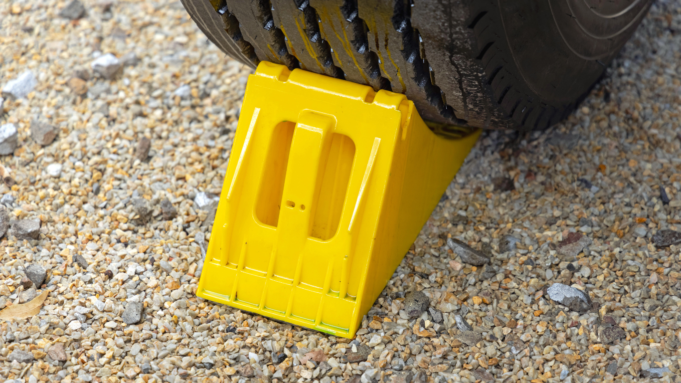 Yellow wheel chock wedged under a car tire on gravel.
