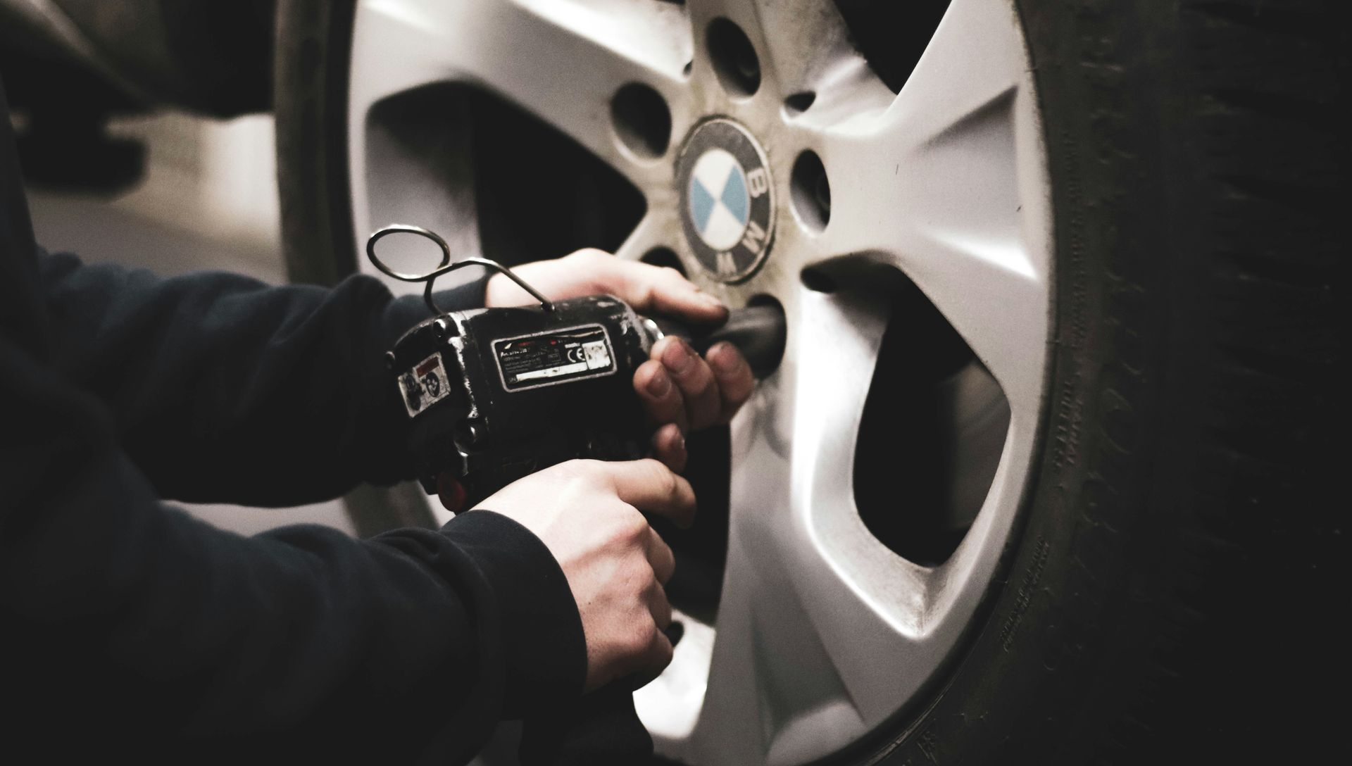 A pair of hands uses a black power tool to tighten a lug nut on a silver BMW wheel.