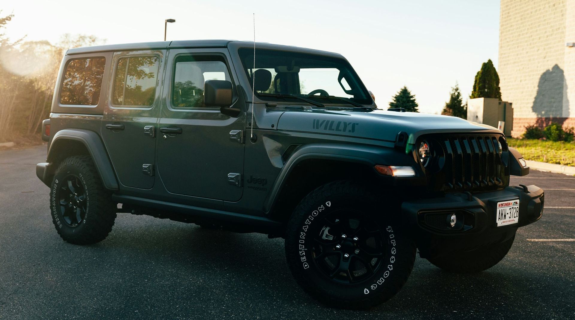 Dark green Jeep Wrangler Willys parked on a road, lit by sunlight.