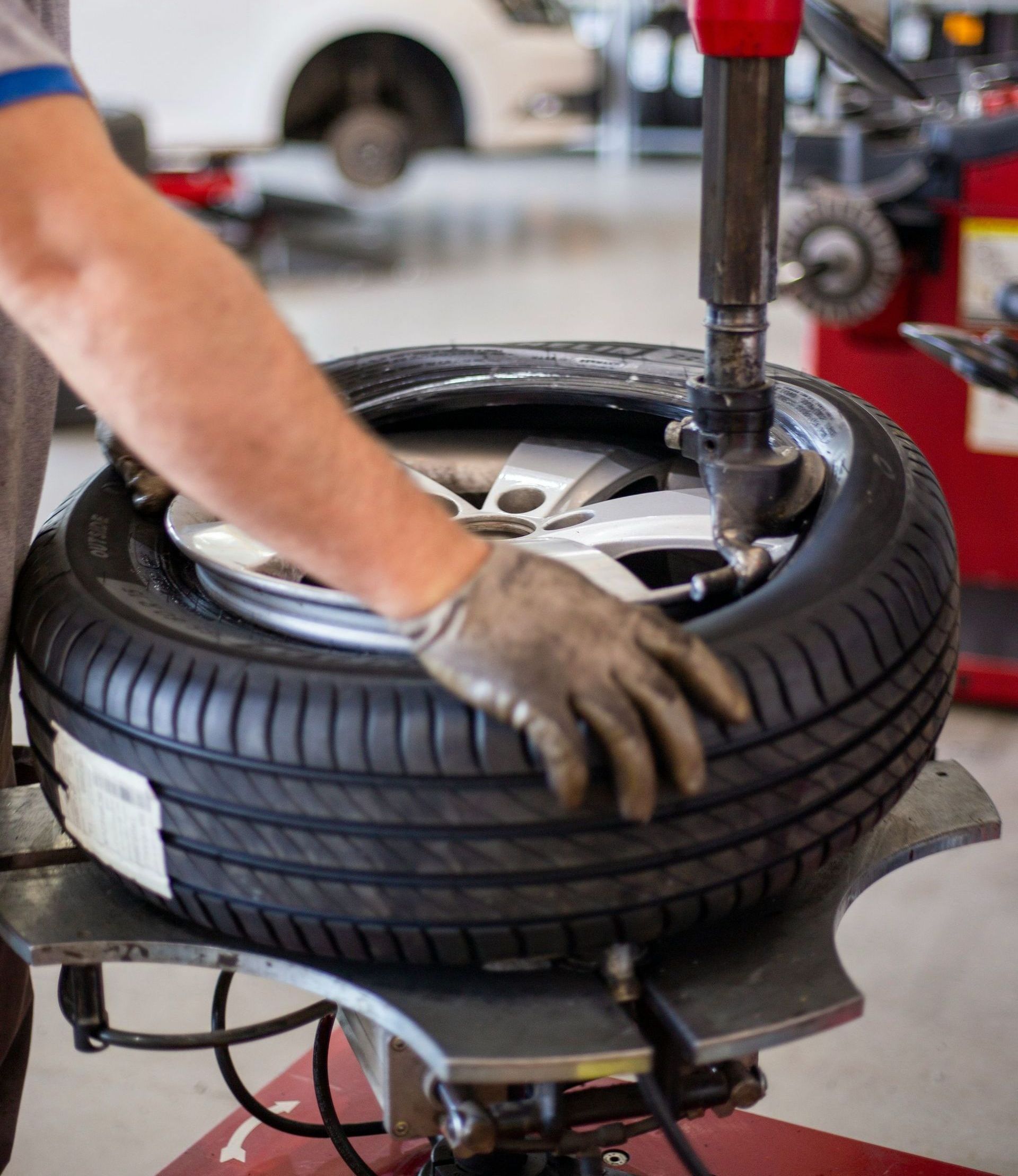 A mechanic using a tire machine to change a car tire. The person is wearing gloves.