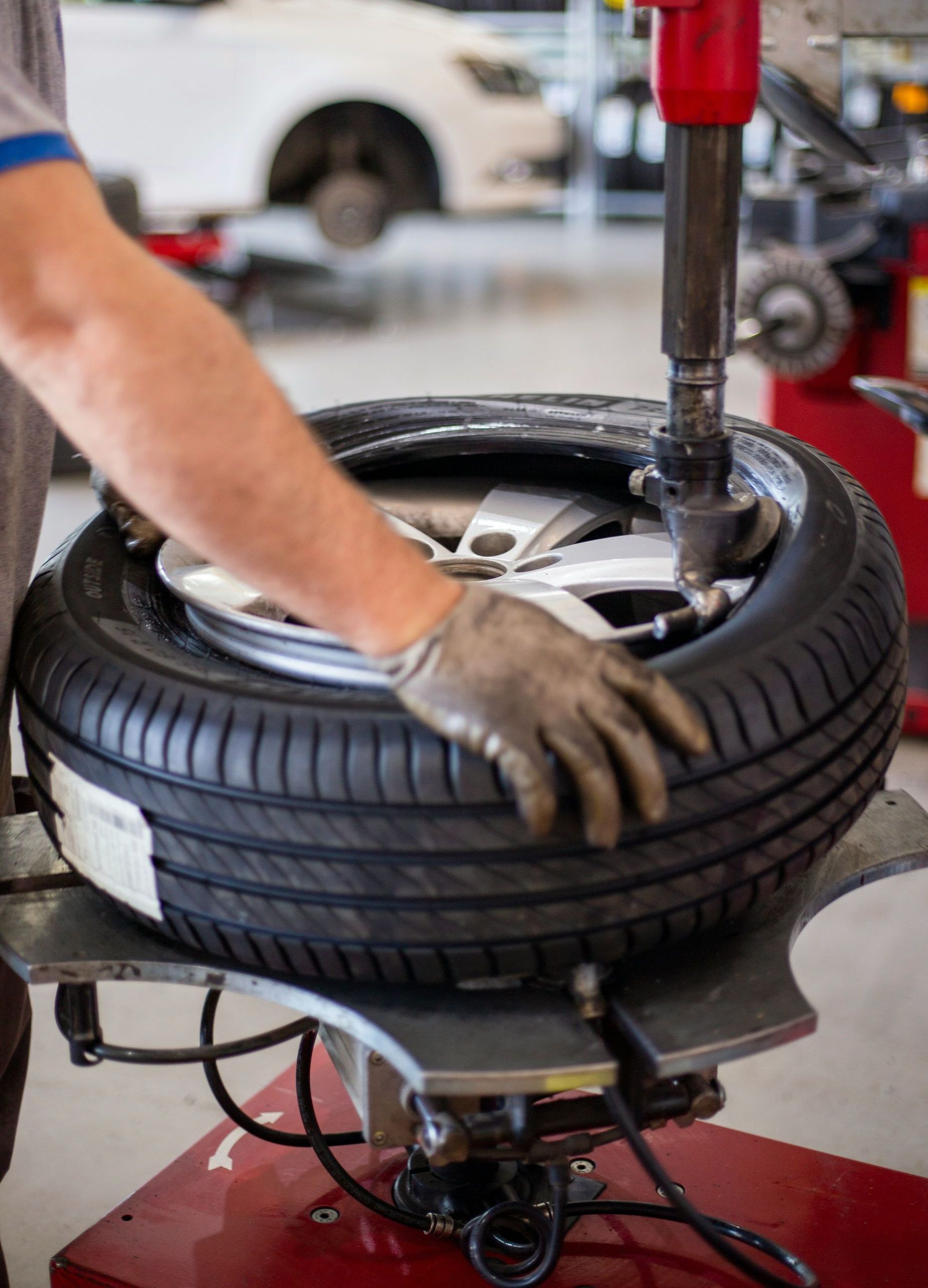 A mechanic using a tire machine to change a car tire. The person is wearing gloves.