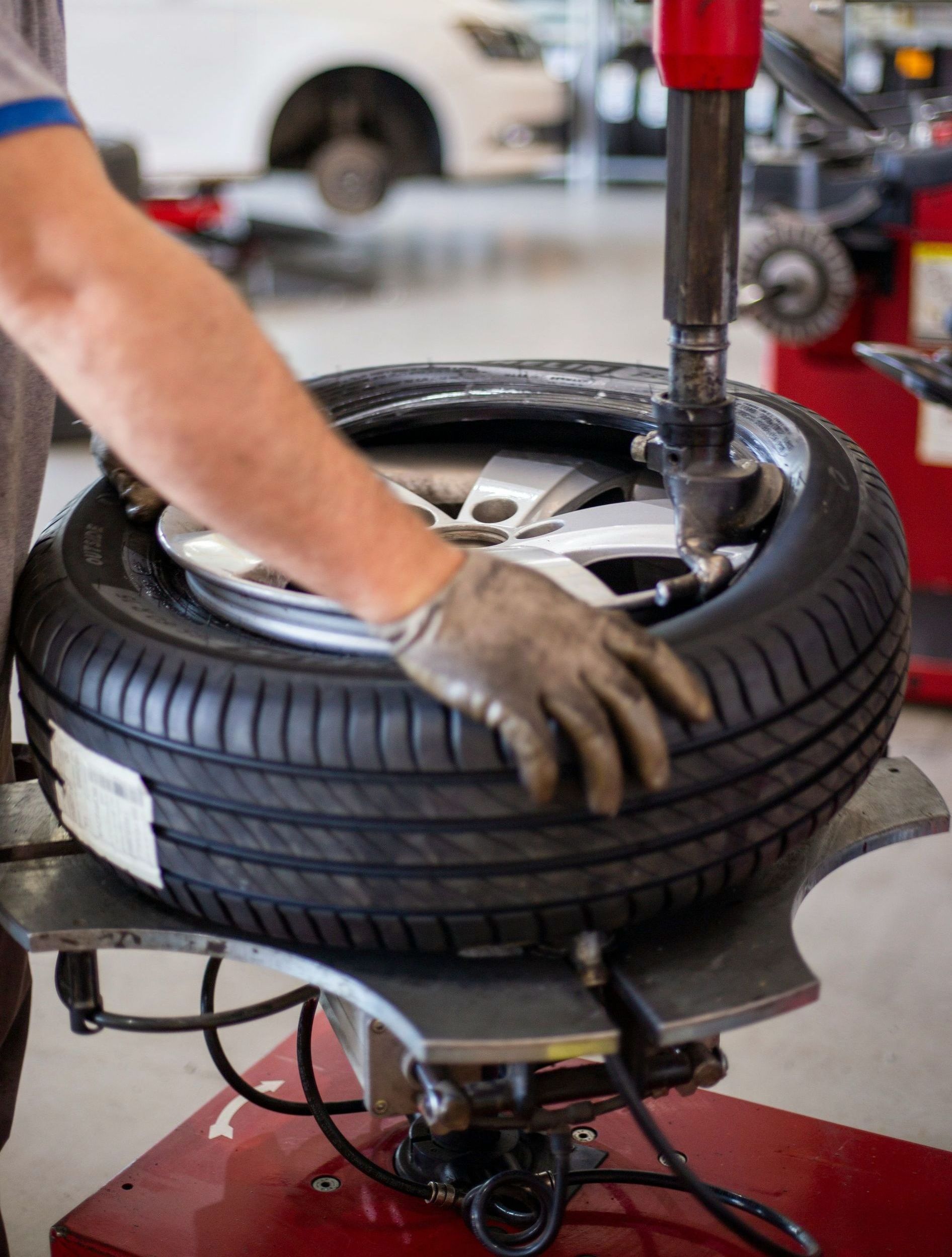 A mechanic using a tire machine to change a car tire. The person is wearing gloves.