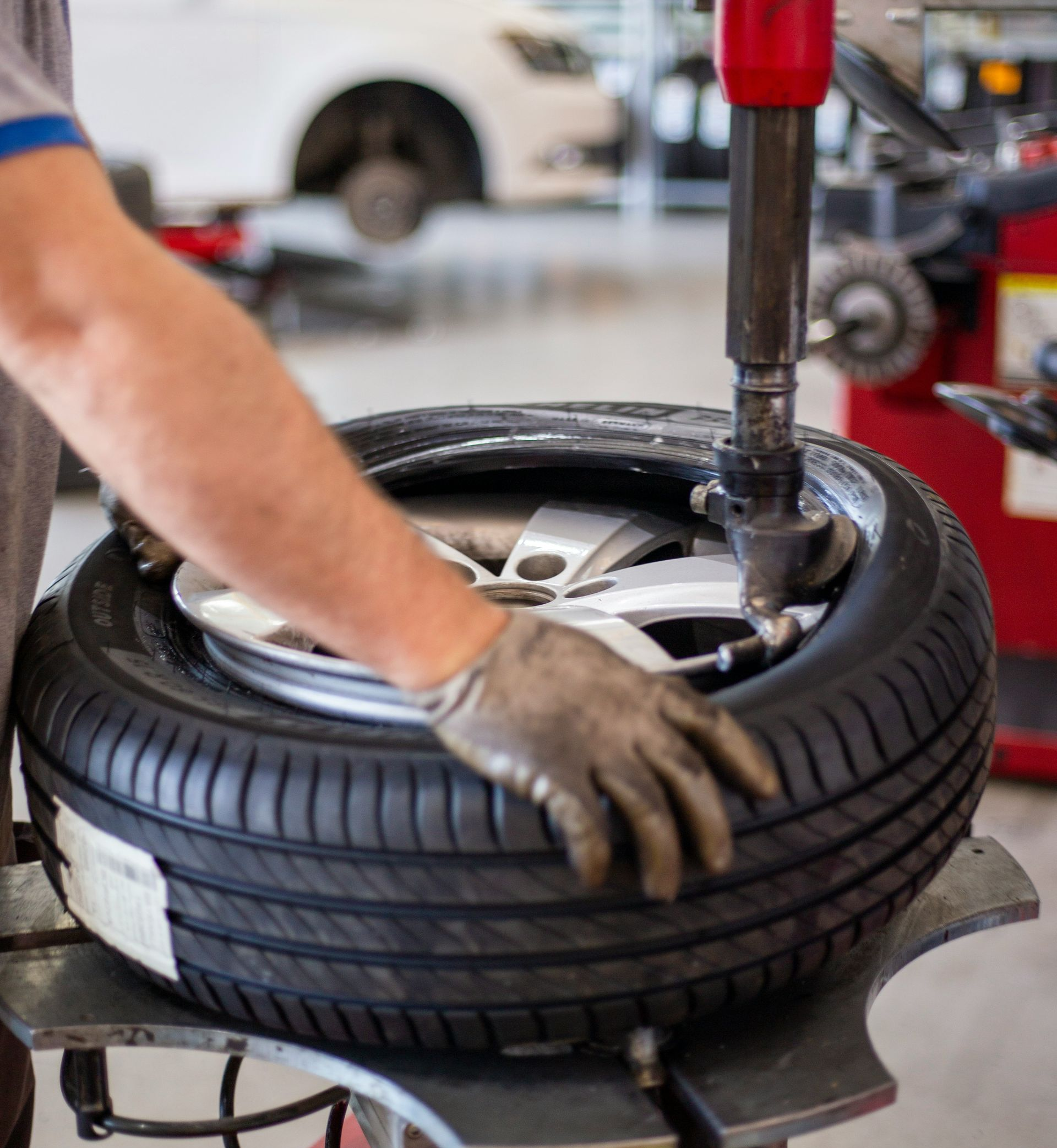 A technician wearing a glove uses a tire changing machine to mount a tire onto a car wheel in a workshop.