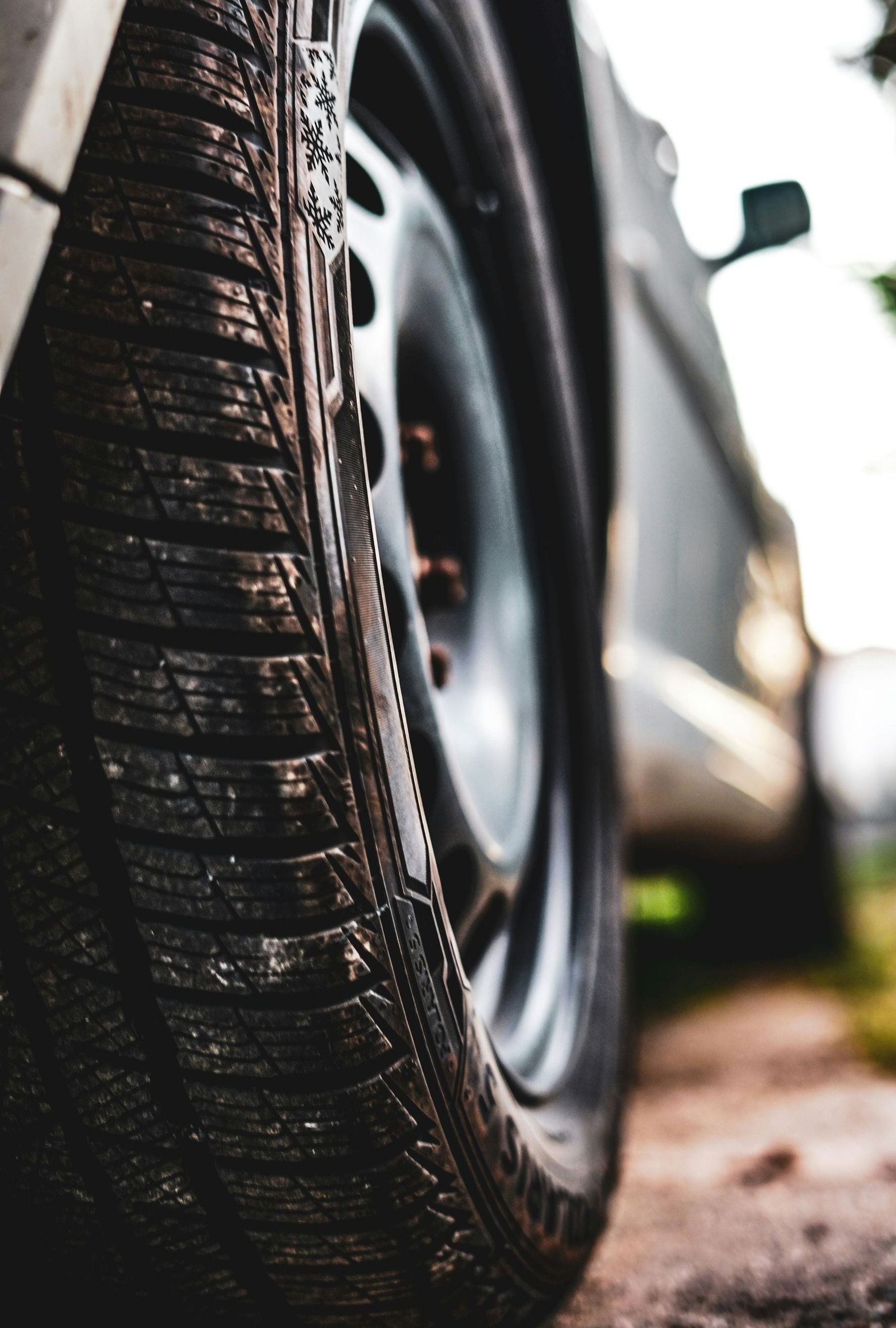 Close-up of a car tire on a dusty road, showing tread detail. Gray car body in background.