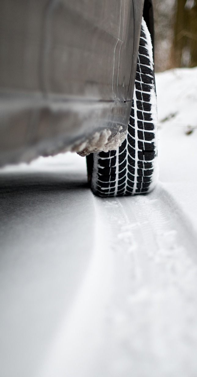 Car tire in snow, leaving a track. Black tire tread, white snow.