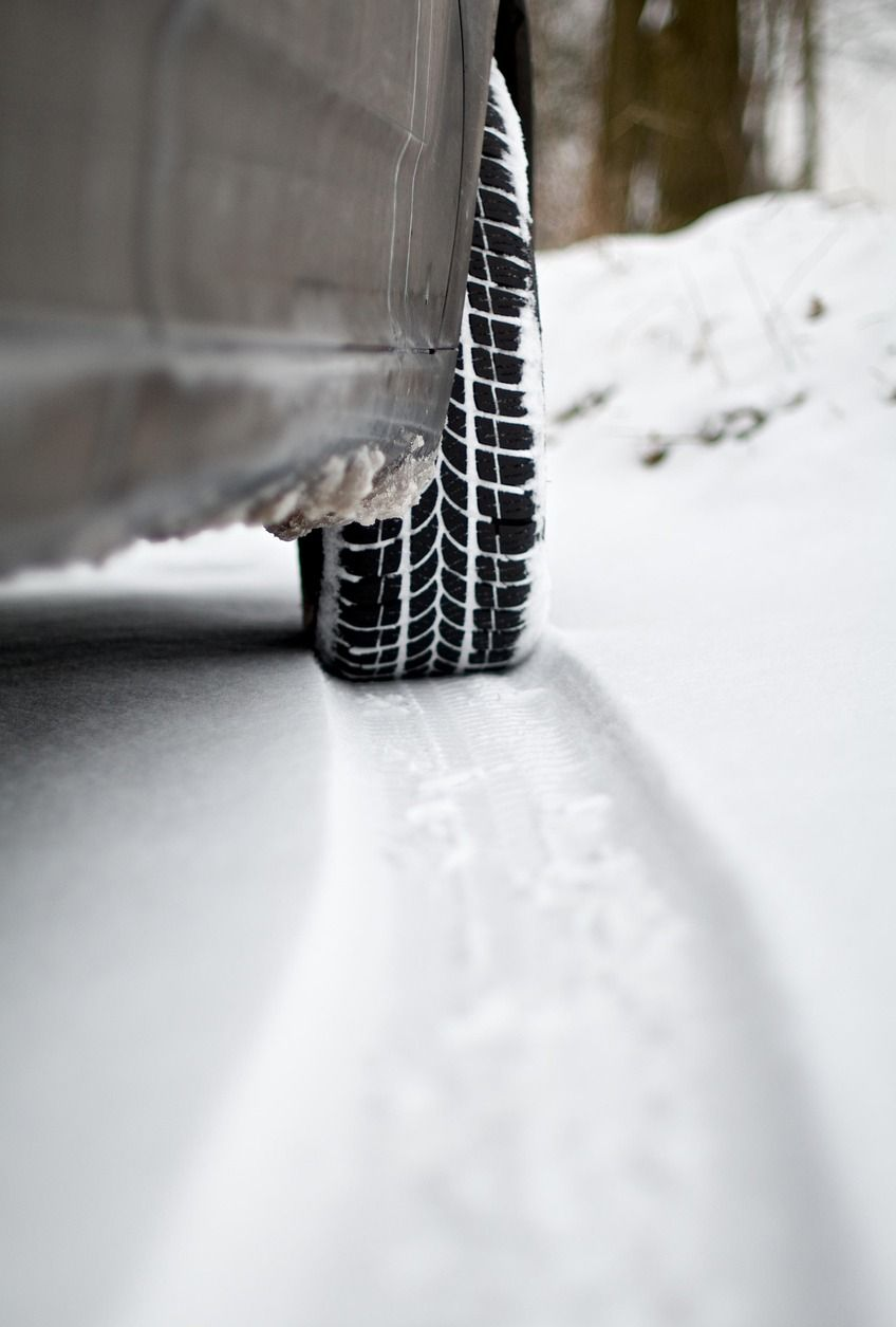Car tire in snow, leaving a track. Black tire tread, white snow.