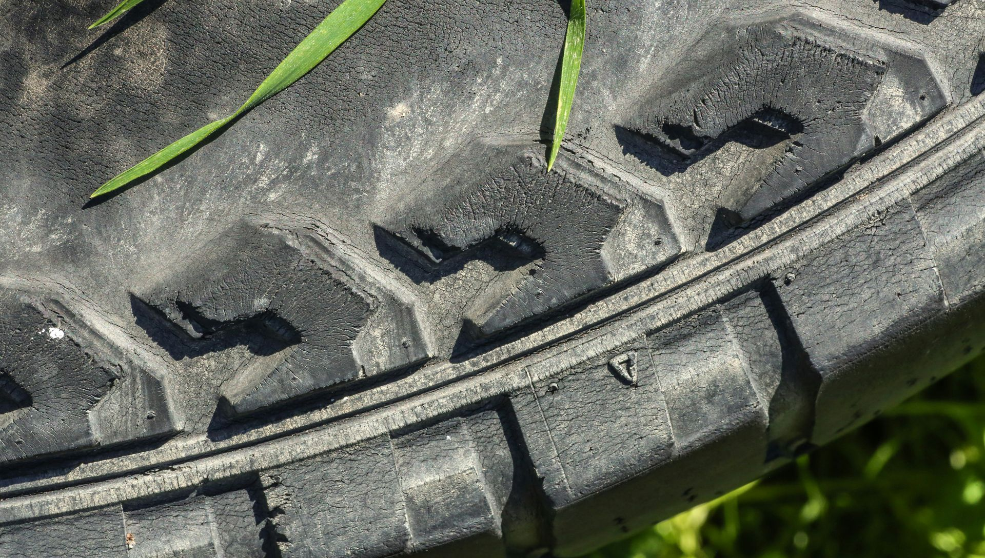 A close-up view of a worn, black tire tread with a few blades of green grass resting on its surface.