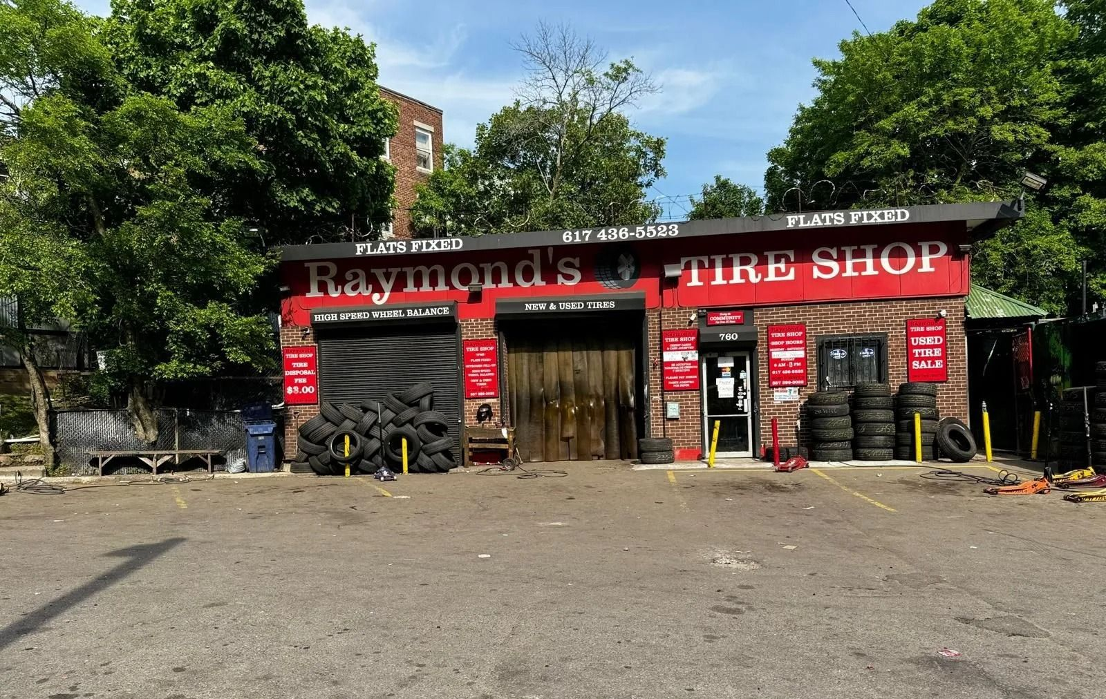 Raymond's Tire Shop storefront with tires displayed, brick facade, red sign, open garage, parked tires.