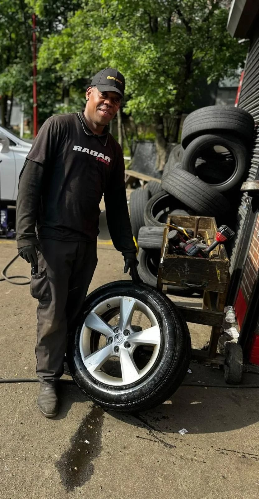 Mechanic points at a car tire in a shop. Tires stacked nearby.