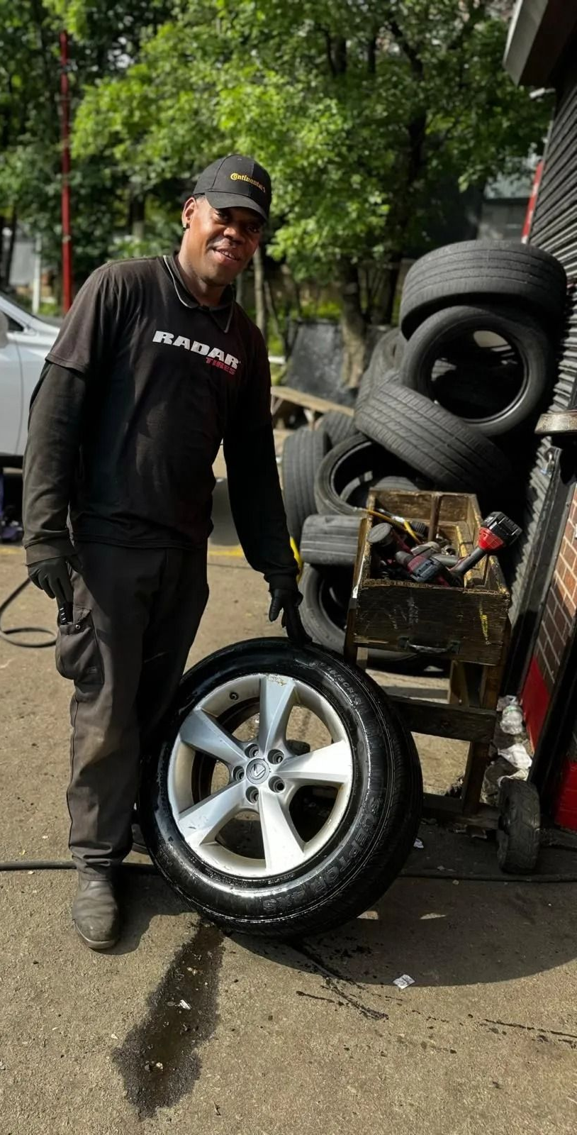 Mechanic points at a car tire in a shop. Tires stacked nearby.