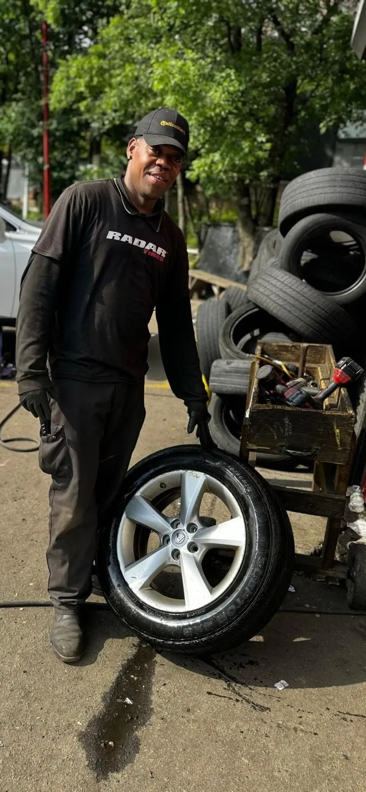 Mechanic points at a car tire in a shop. Tires stacked nearby.
