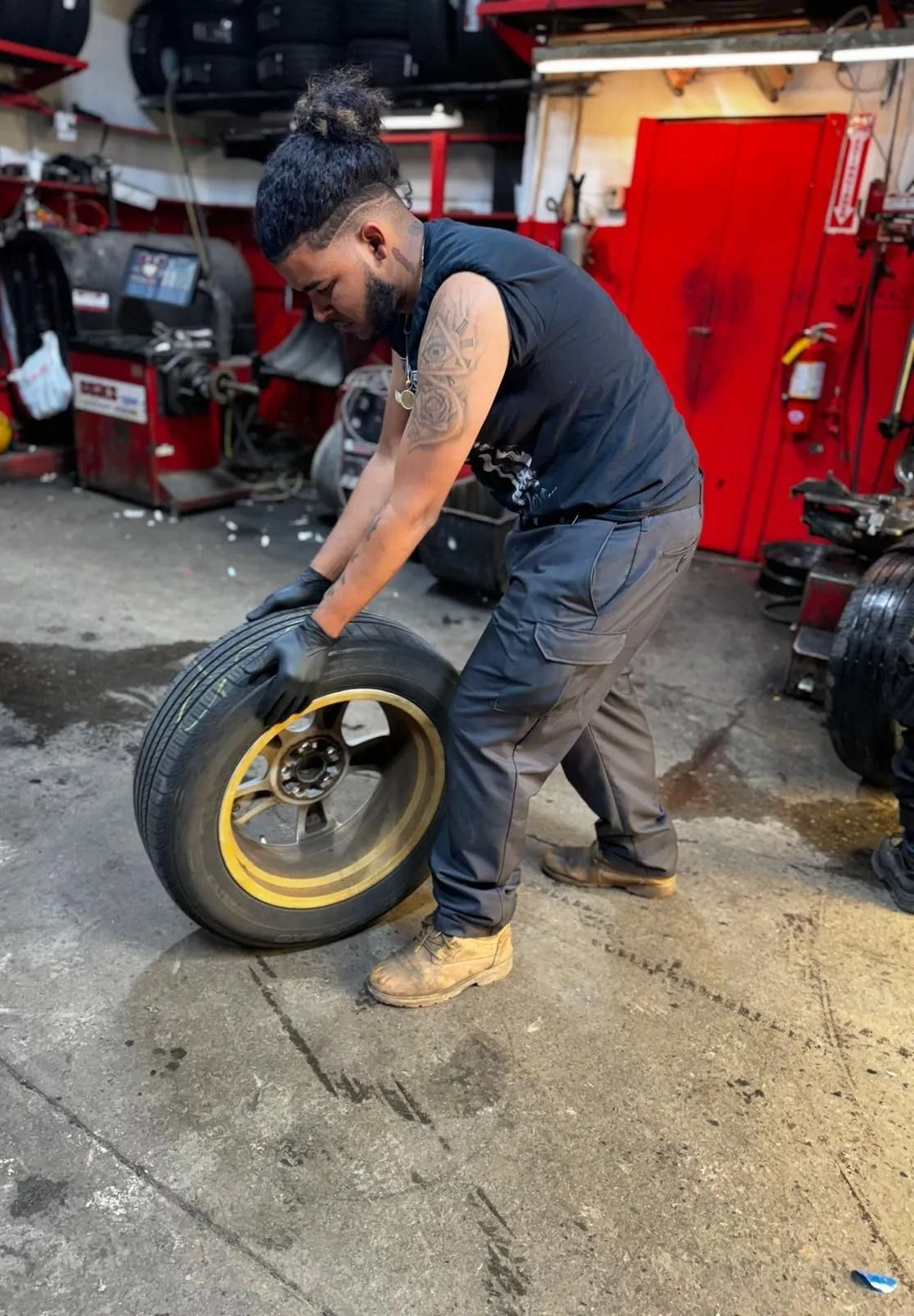 Man in garage, lifting a tire with yellow rim.