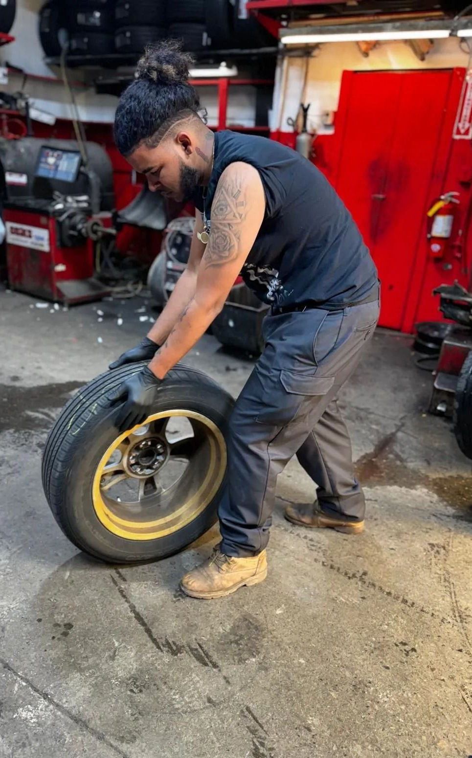 Man in garage, lifting a tire with yellow rim.