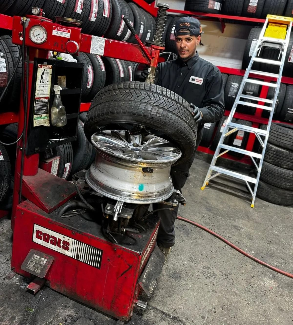 Mechanic changing a tire on a machine, in a tire shop. Red machine, tires in background.
