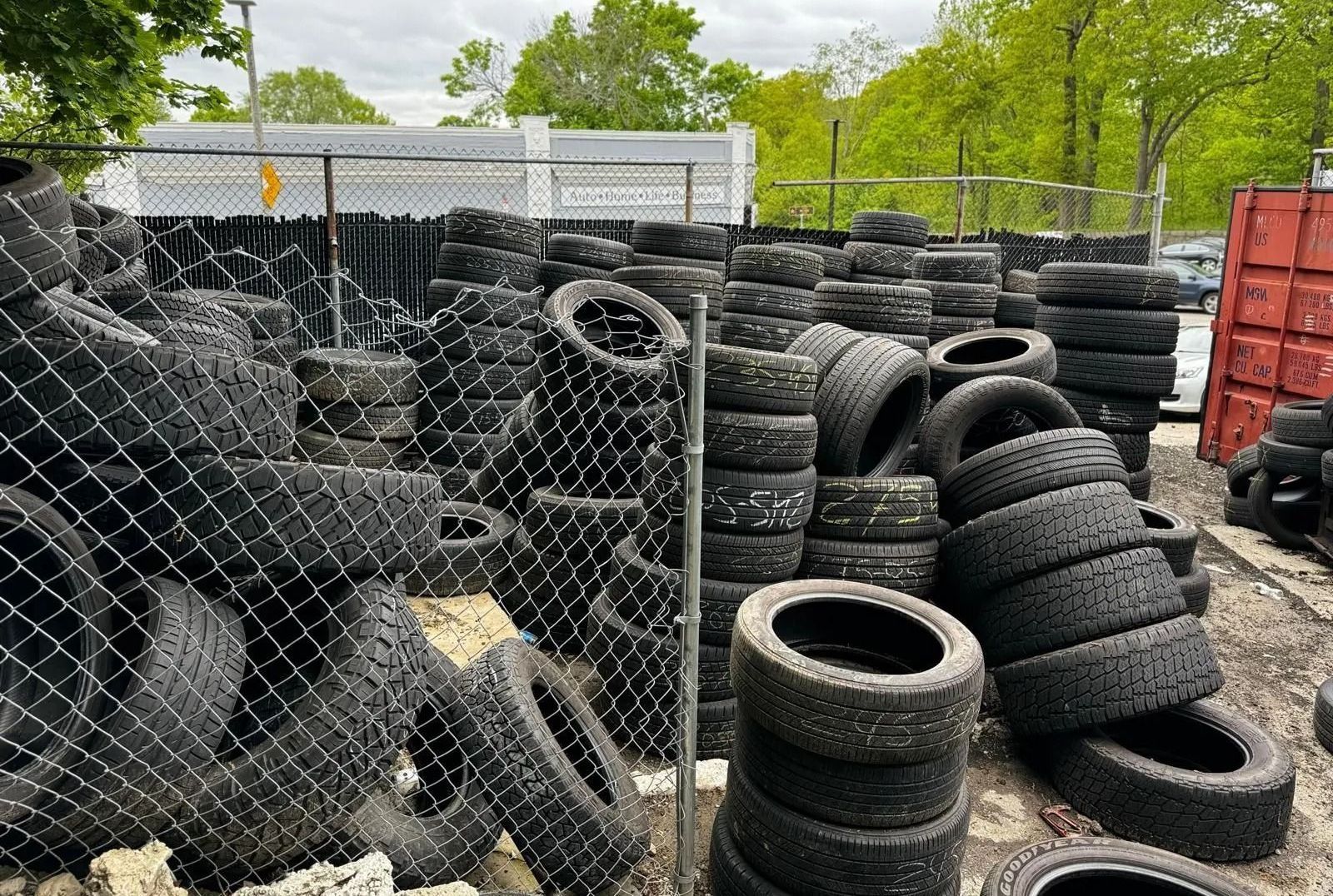 Piles of used tires, mostly black, stacked in a fenced outdoor area.
