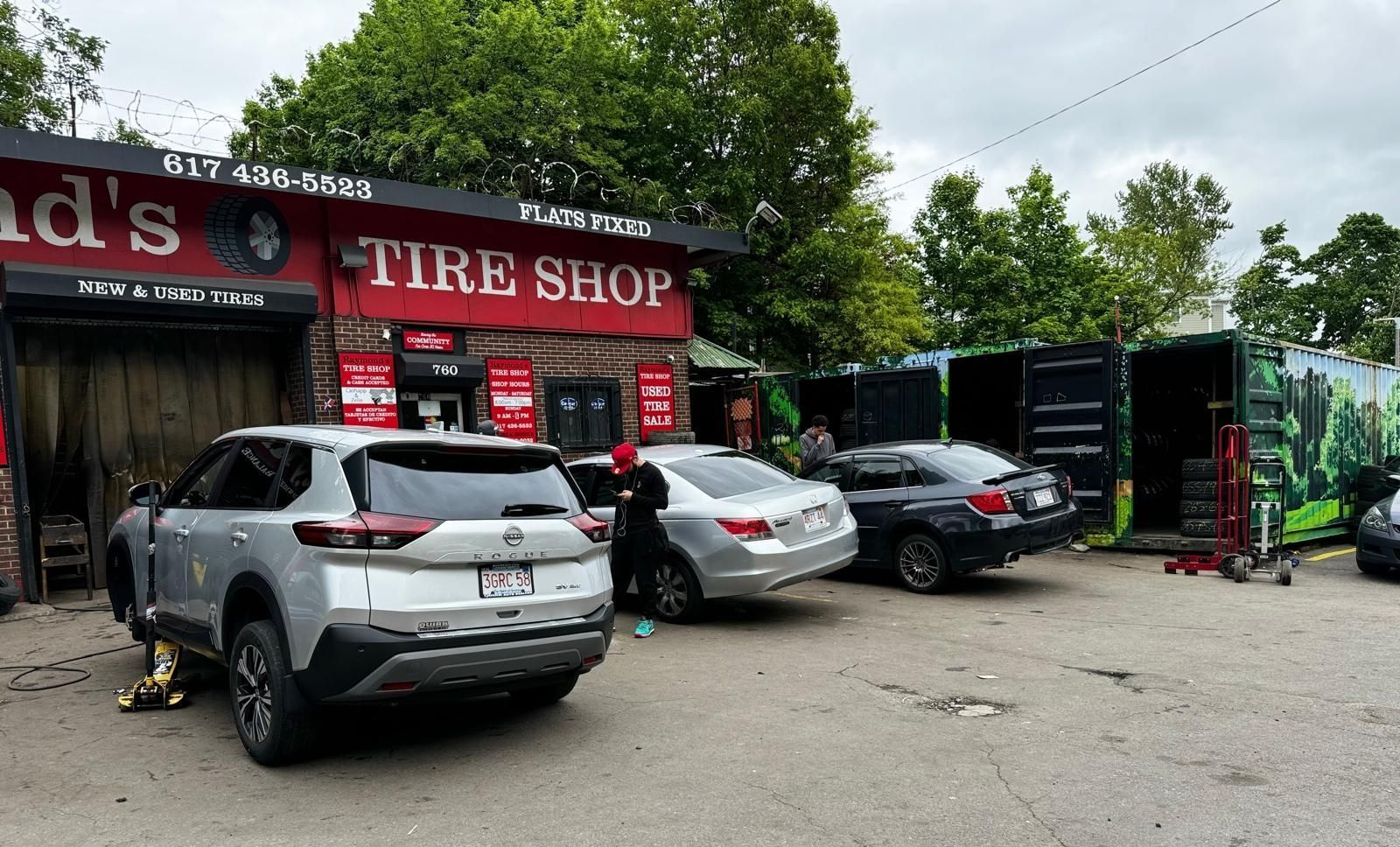 A tire shop with cars being serviced; silver SUV on jack, other cars parked outside.
