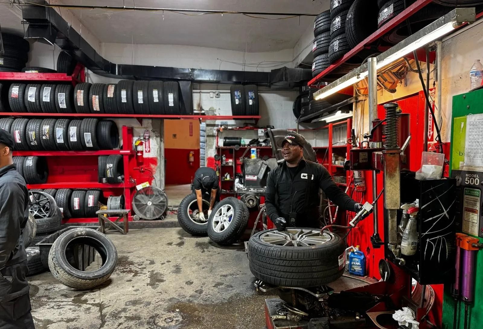 Inside a tire shop, workers repair a tire. Tires stacked on shelves and the floor.