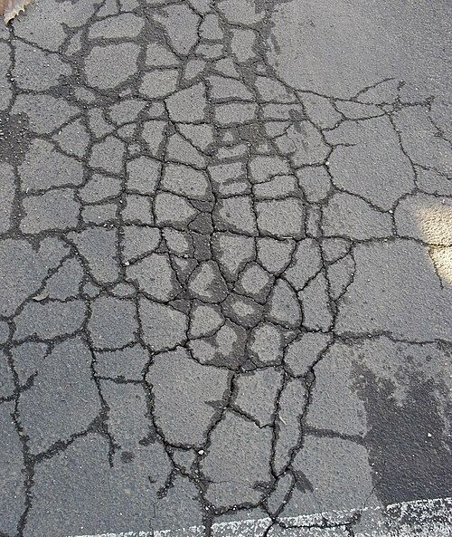 Close-up of gray asphalt pavement featuring an extensive network of interlocking alligator cracking.