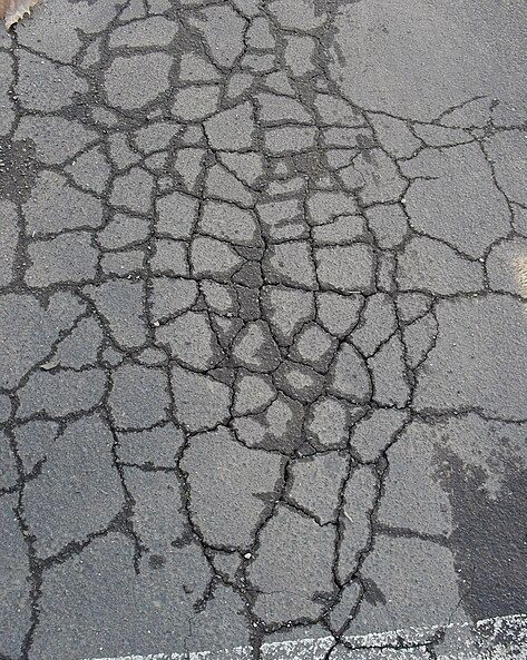 Close-up of gray asphalt pavement featuring an extensive network of interlocking alligator cracking.