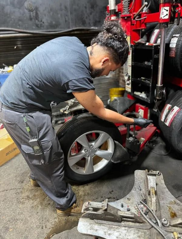 Mechanic changing a tire using a machine in a garage. The person is wearing gray pants and a blue shirt.