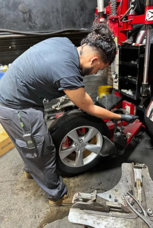 Mechanic changing a tire using a machine in a garage. The person is wearing gray pants and a blue shirt.