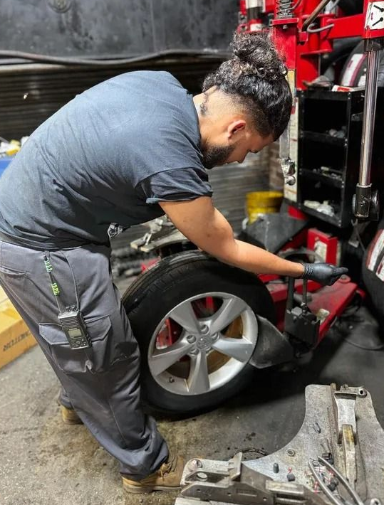 Mechanic changing a tire using a machine in a garage. The person is wearing gray pants and a blue shirt.