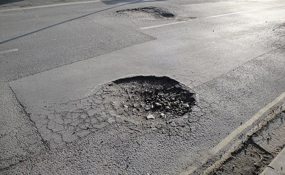 A deep, dark pothole in the asphalt surface of a paved road.