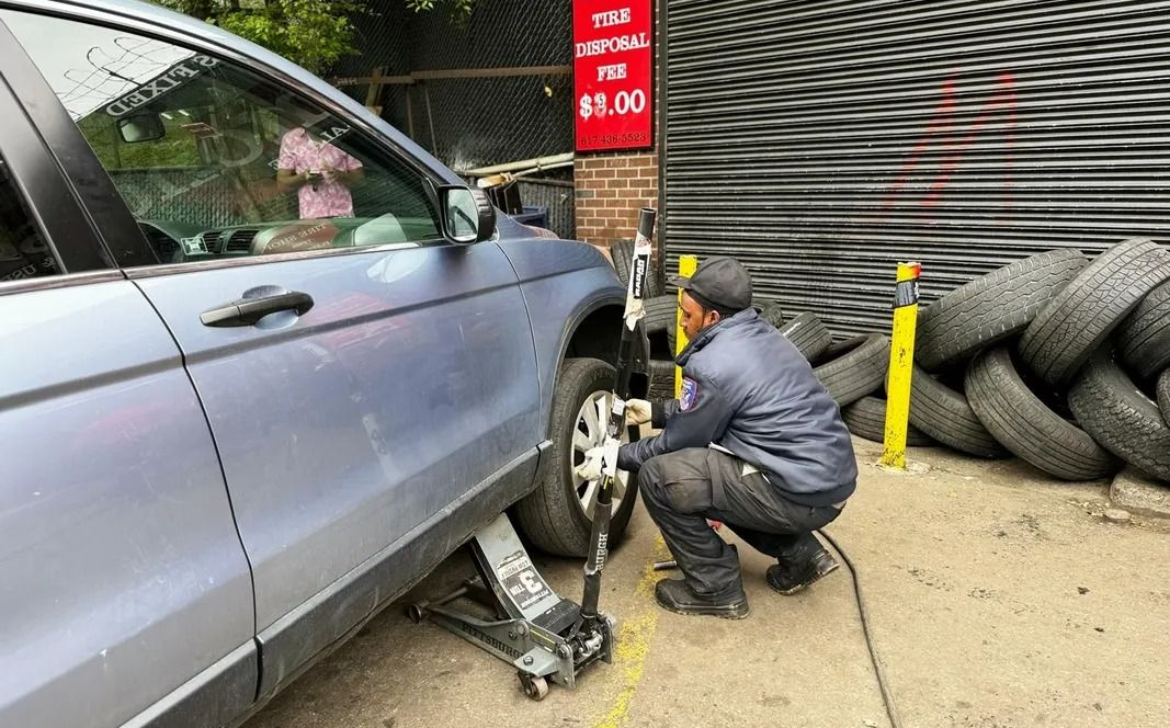 A mechanic changing a tire on a silver car outside a garage.