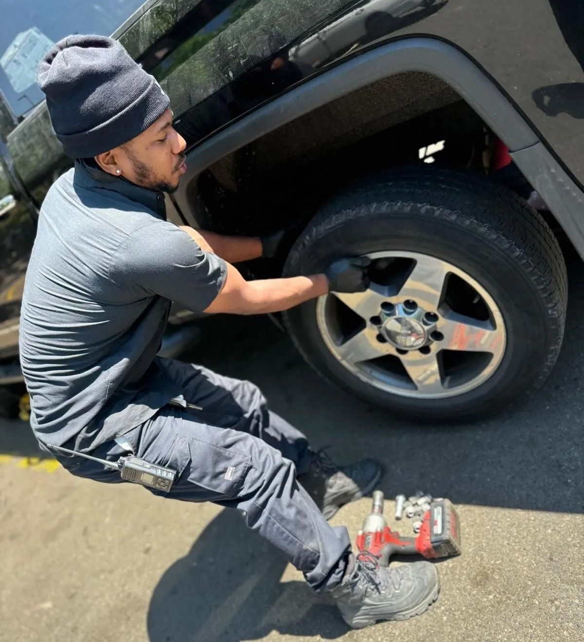 A person in dark clothing changes a tire on a black vehicle, with tools nearby.