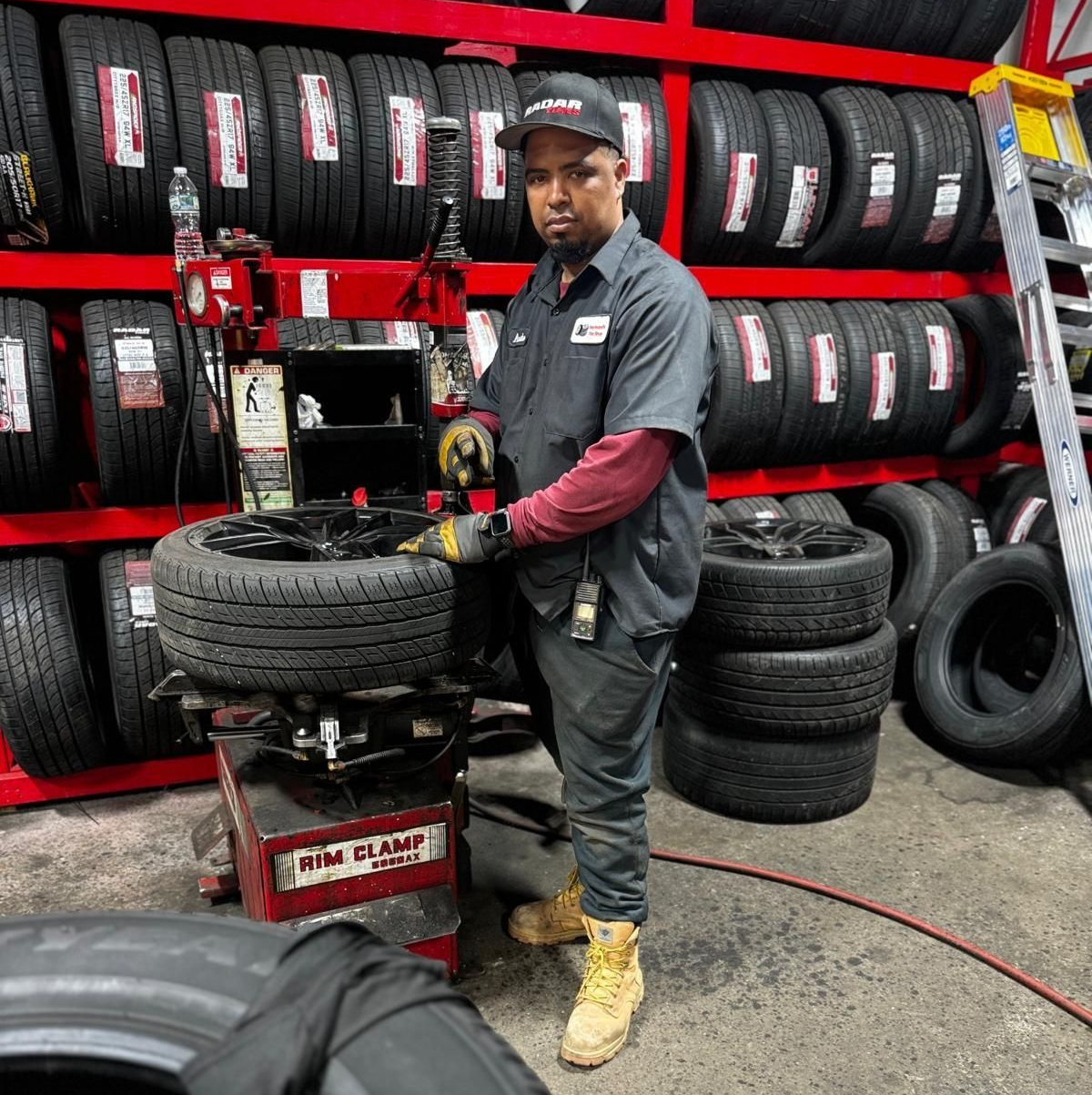 Man in a mechanic shop using a tire machine, with shelves of tires in the background.