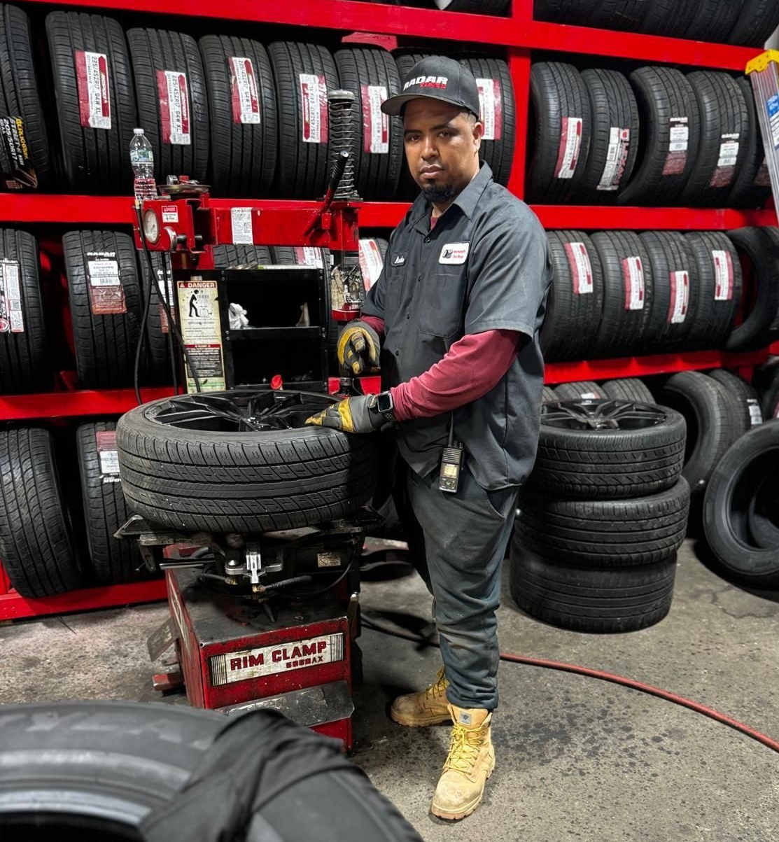 Man in a mechanic shop using a tire machine, with shelves of tires in the background.
