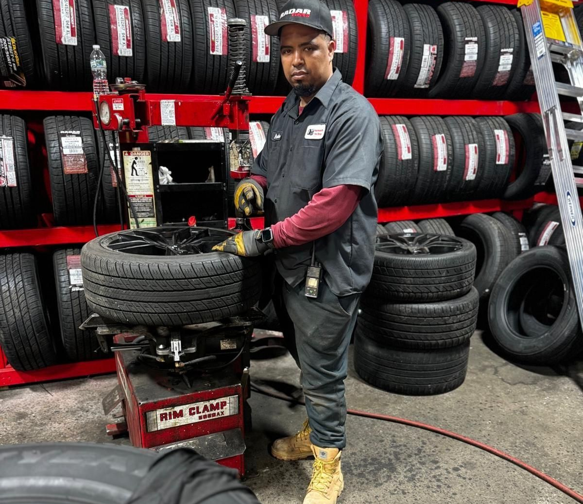 Man in a mechanic shop using a tire machine, with shelves of tires in the background.