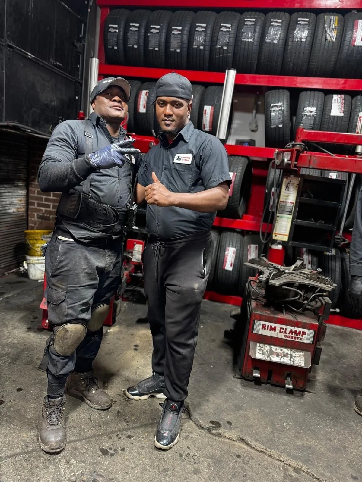 Two auto mechanics, one with a peace sign, in a tire shop. Tires line the wall.