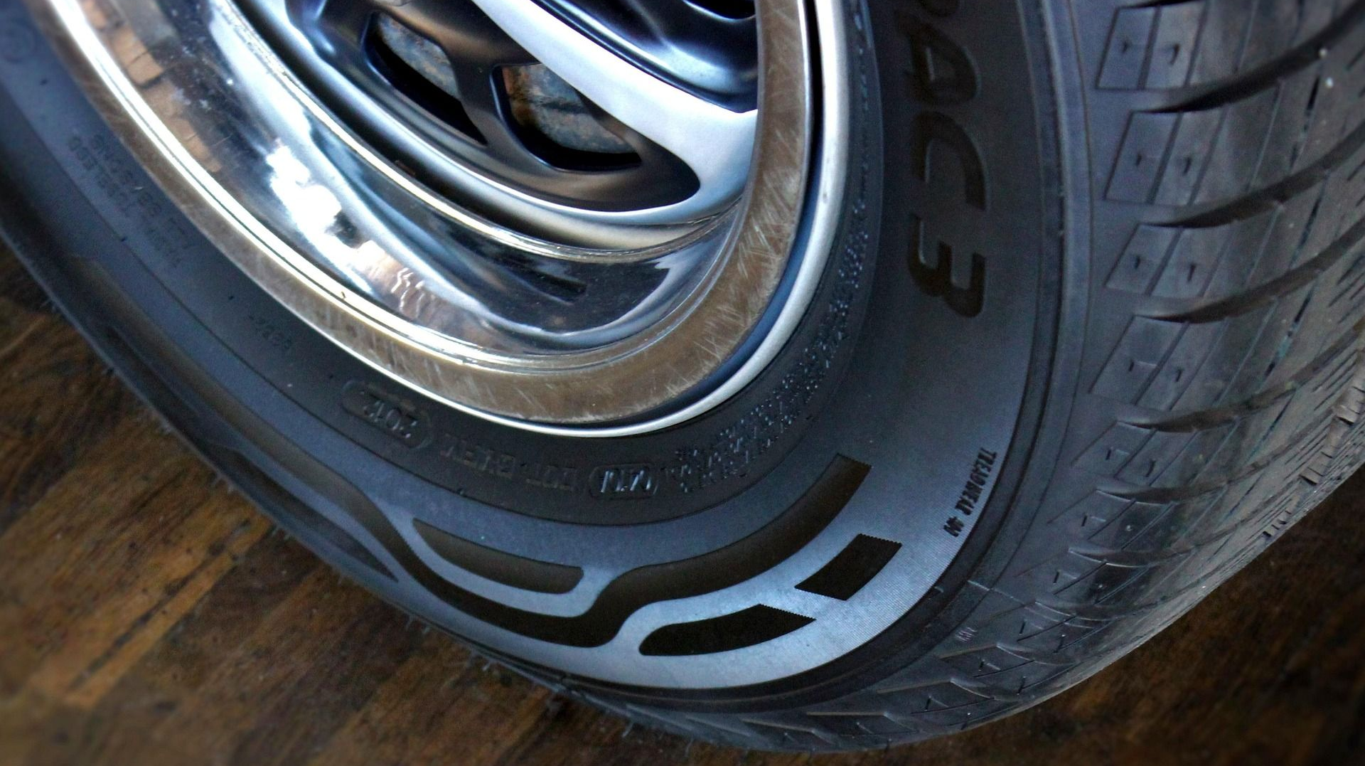 Close-up of a shiny car wheel and tire on a wooden floor, with a stylized design on the sidewall.