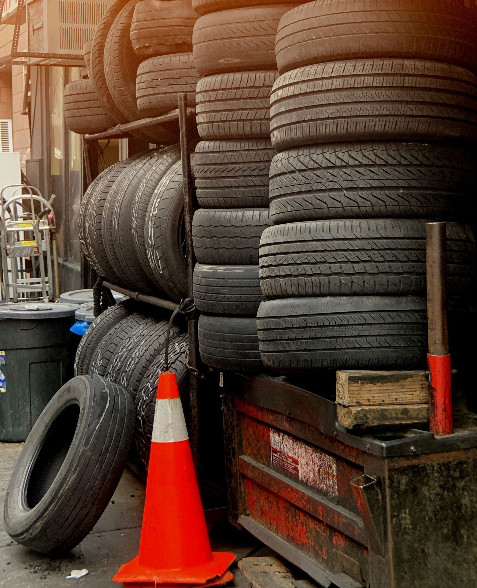 Stack of used tires, a traffic cone, and a toolbox are in front of a shop.