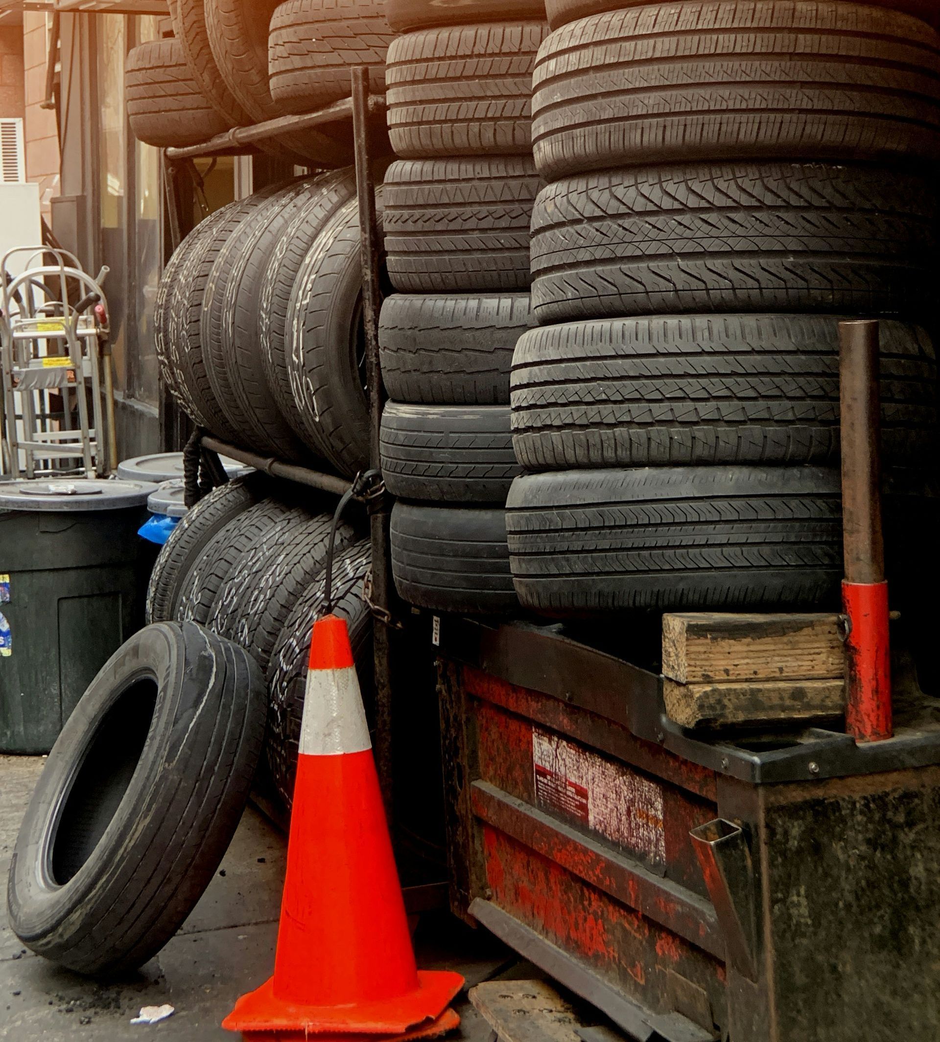 Stack of used tires, a traffic cone, and a toolbox are in front of a shop.