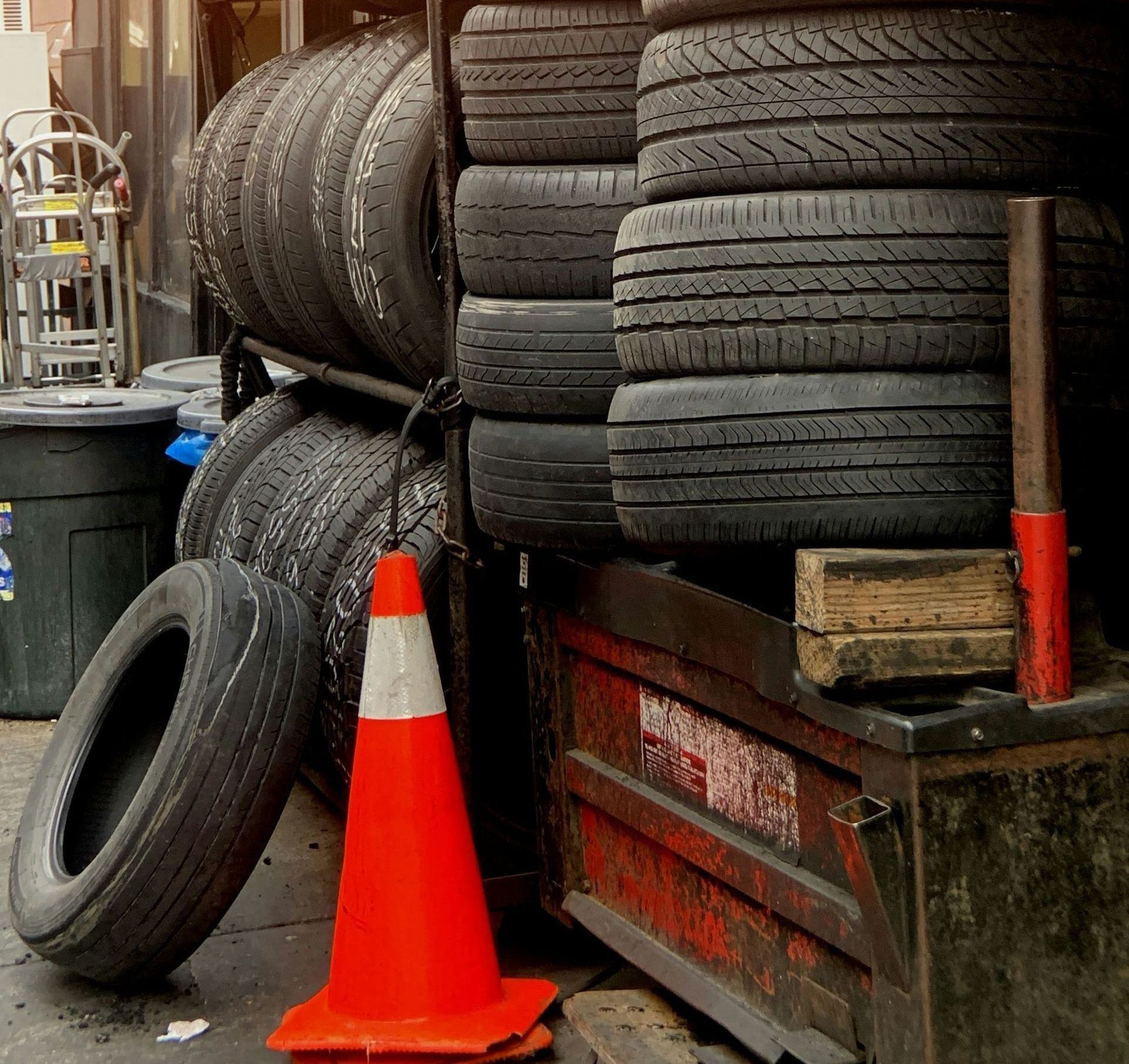 Stack of used tires, a traffic cone, and a toolbox are in front of a shop.