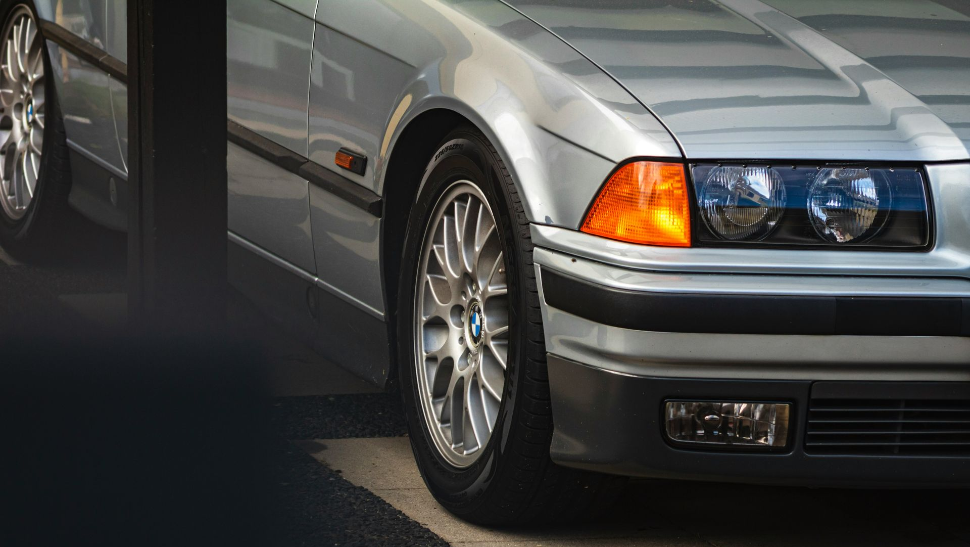 A silver BMW E36 sedan parked on pavement.