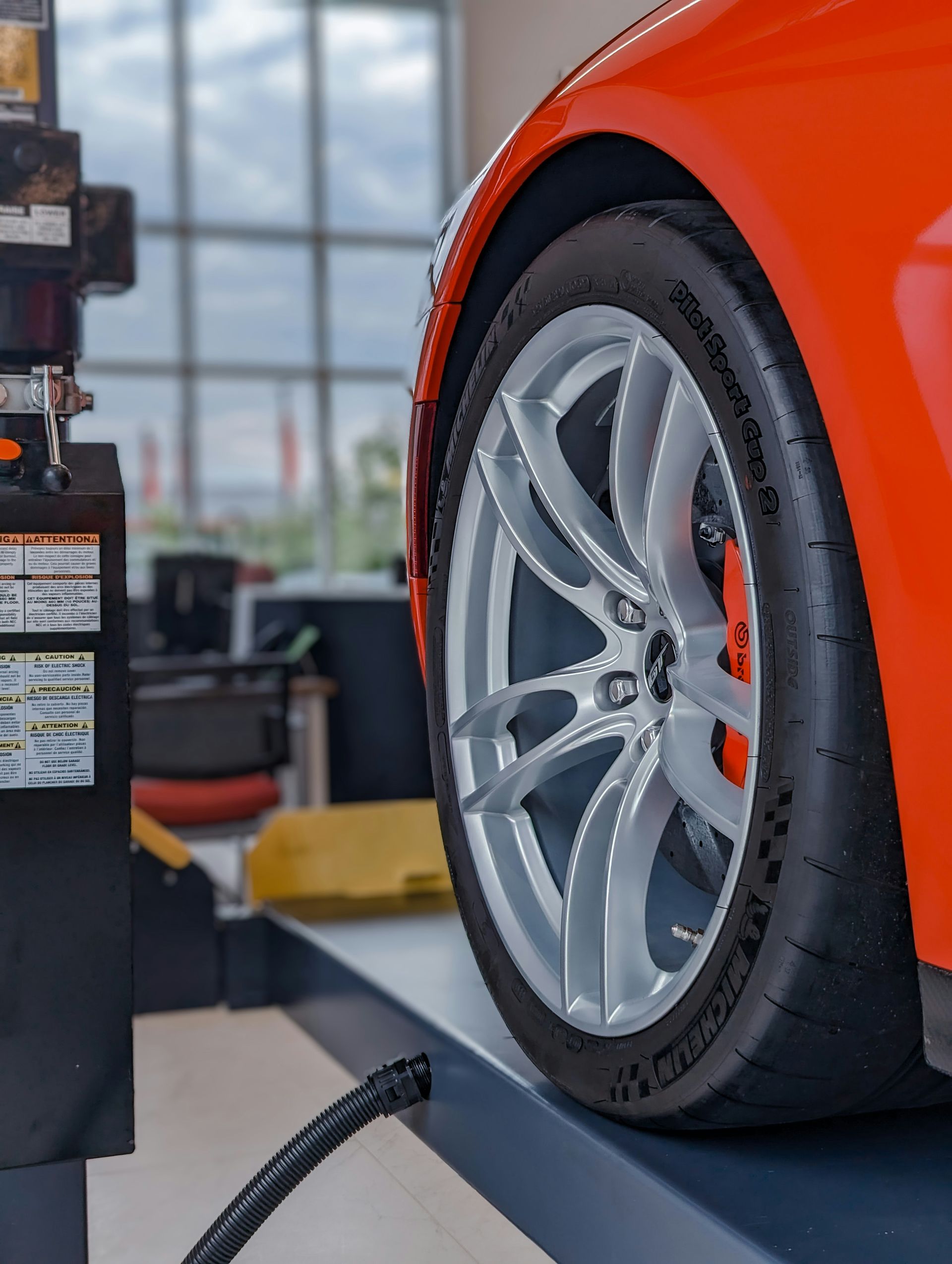 A close-up view of an orange car wheel with a silver rim on a lift inside an auto repair shop.