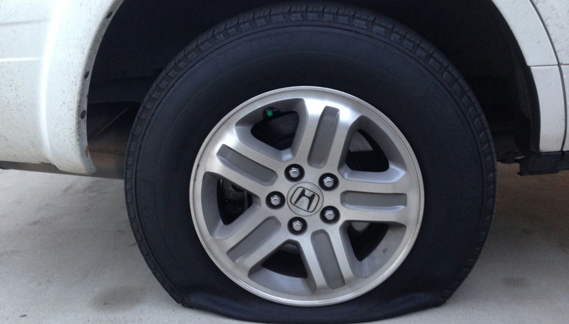 A white vehicle with a flat tire resting on a concrete surface.