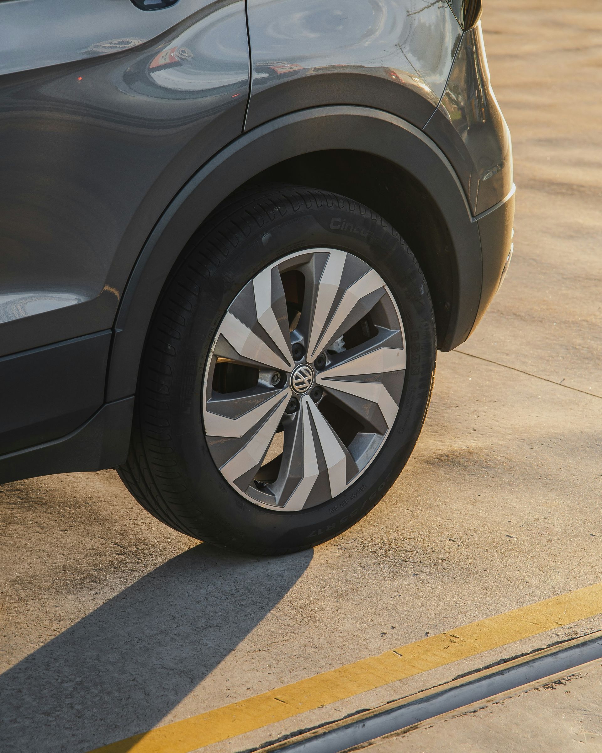 Gray car's rear tire and wheel, with a silver and gray spoke design, parked on concrete.