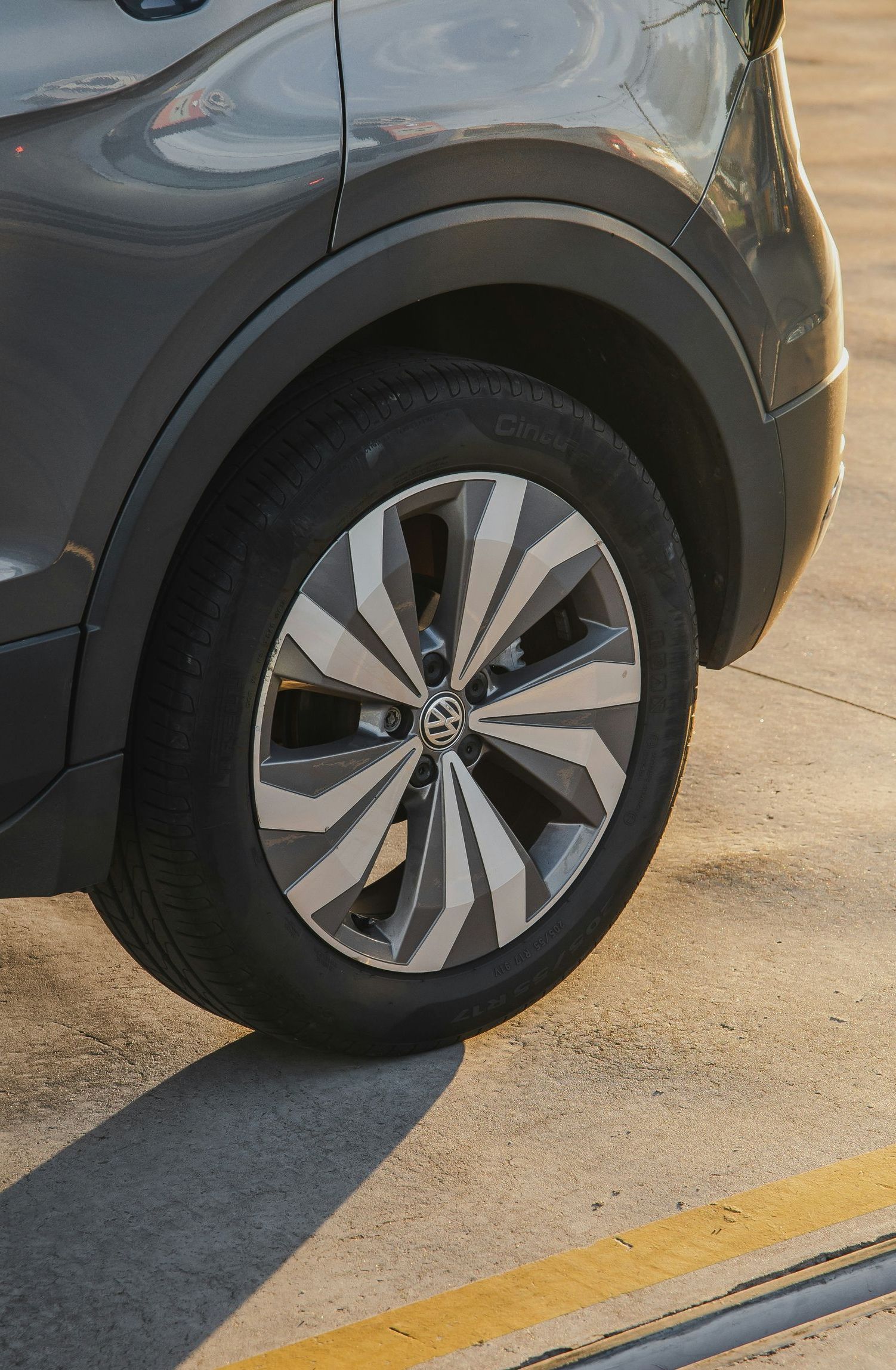 Gray car's rear tire and wheel, with a silver and gray spoke design, parked on concrete.