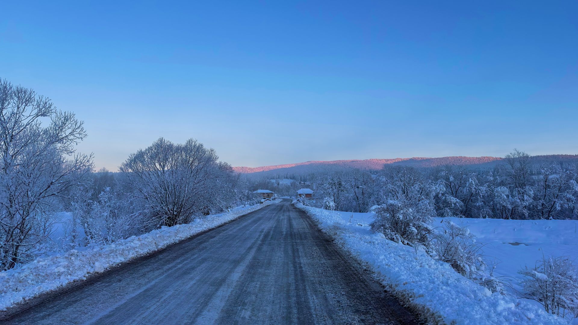Snowy road through a winter landscape with frosted trees and a clear blue sky.