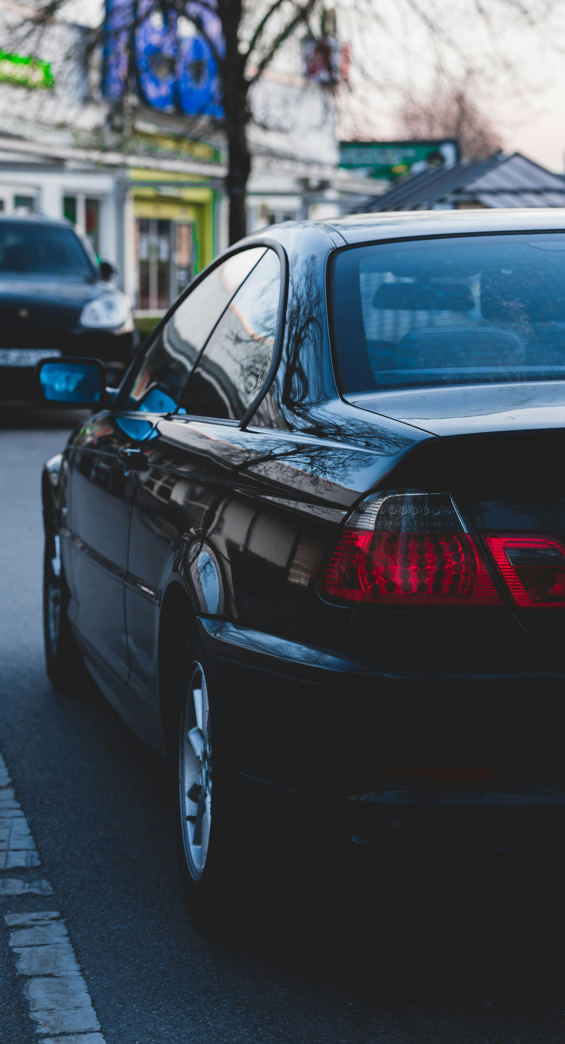 Black car parked on a street; another car visible in the background.