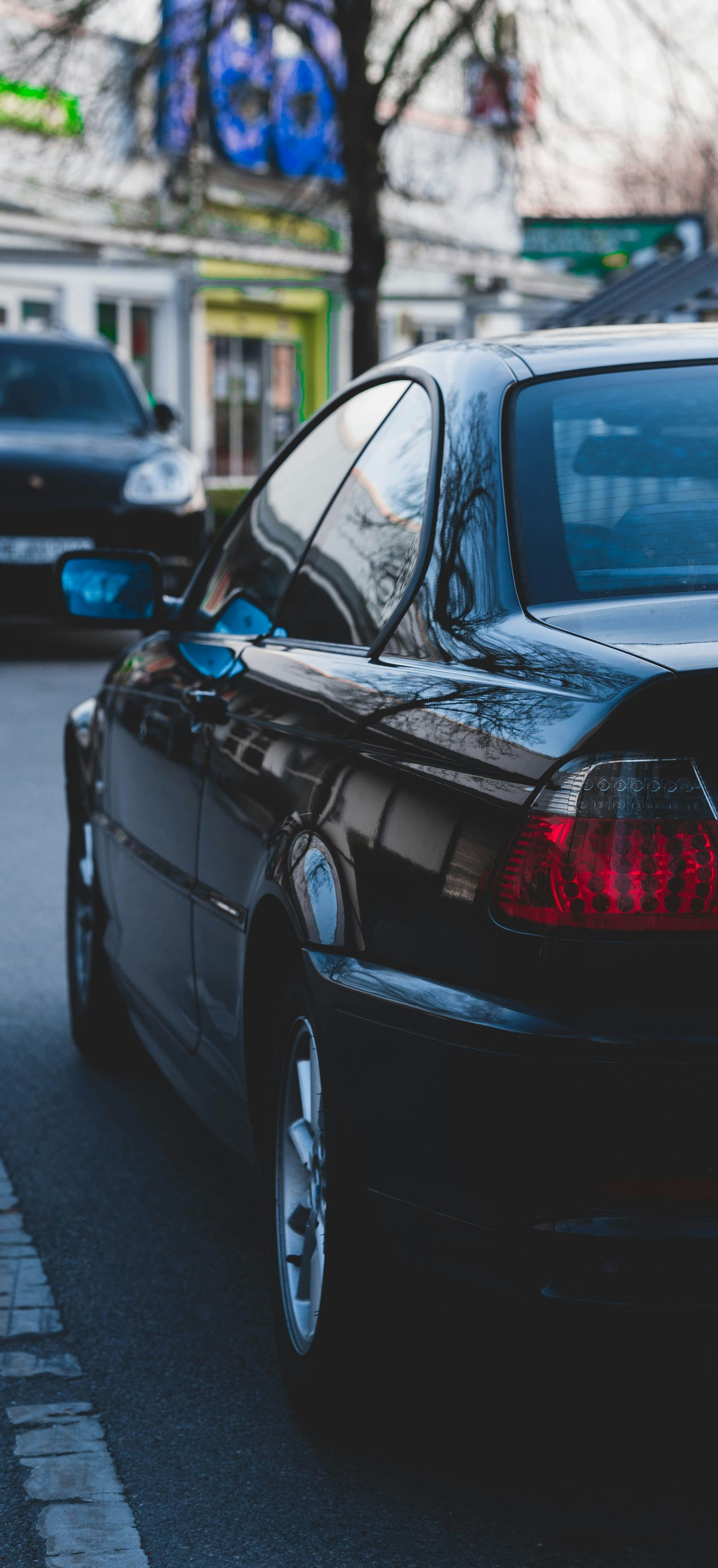 Black car parked on a street; another car visible in the background.