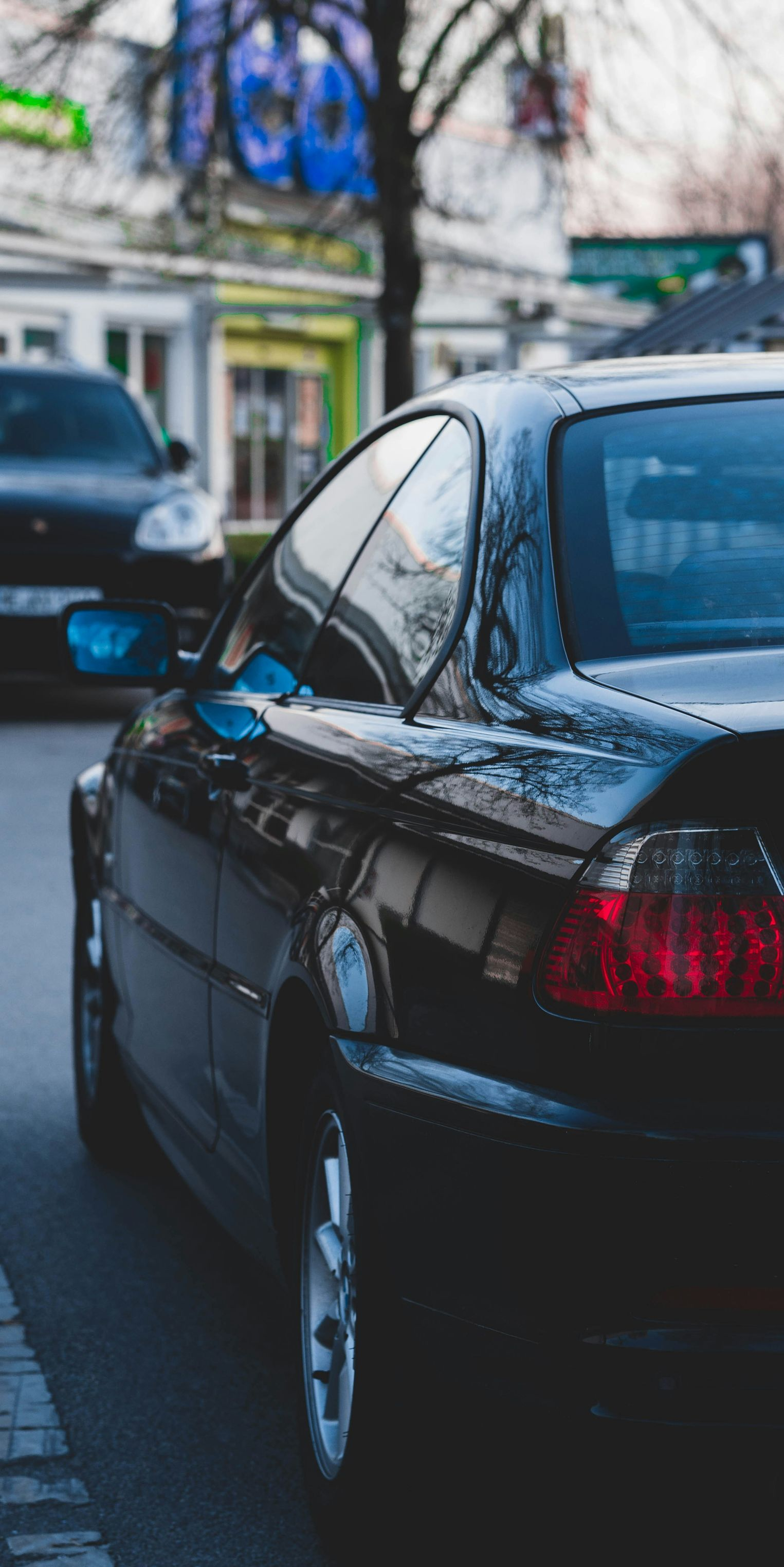 Black car parked on a street; another car visible in the background.