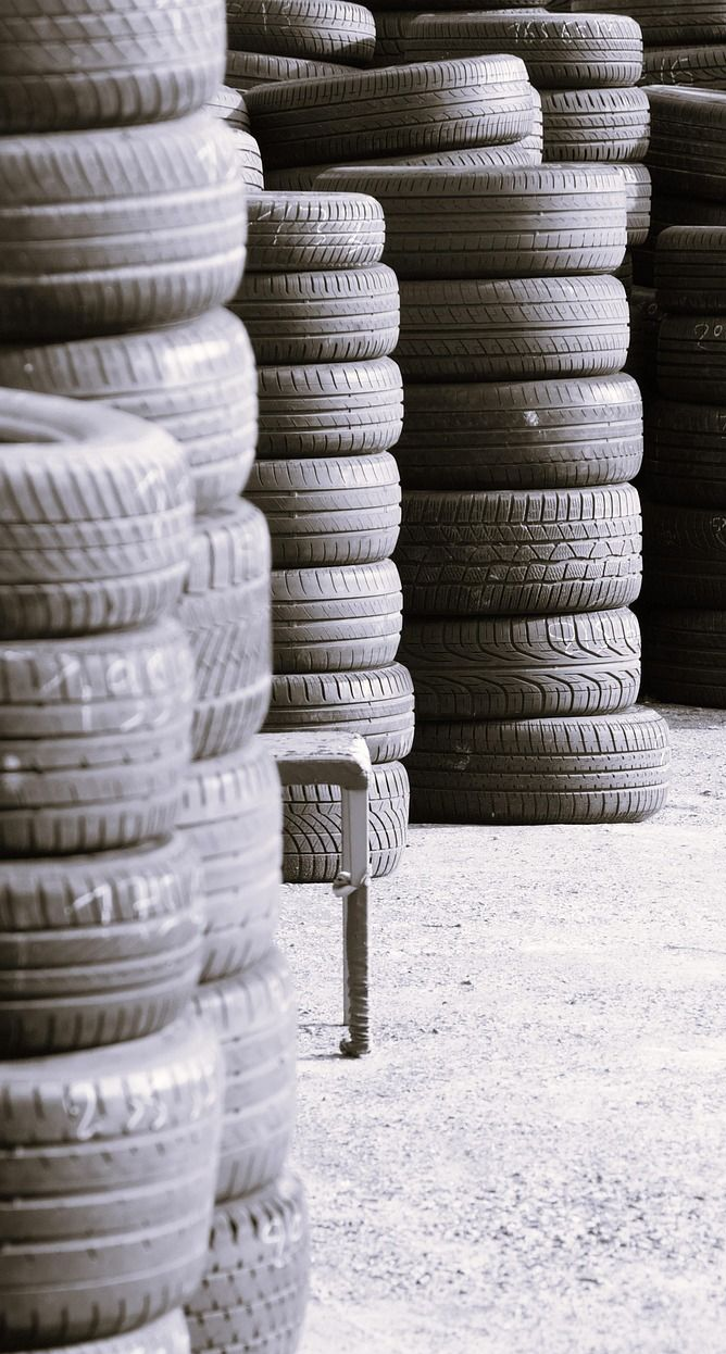 Stacks of used tires in an outdoor setting, arranged vertically, gray tones.